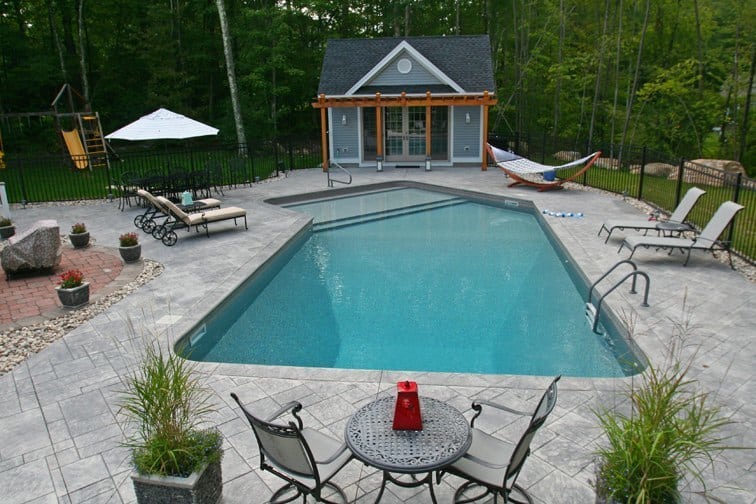 Lazy L style inground swimming pool with custom pool house and pool furniture by Cypress Pools