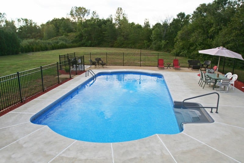 Roman in ground pool in Queensbury, NY with custom pavers, black fence and steps by Cypress Pools