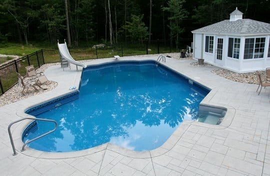 Lazy L style custom inground swimming pool with a custom pool house and water slide by Cypress Pools