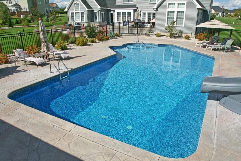 Lazy L style custom inground swimming pool with a black fence, steps and water slide by Cypress Pools