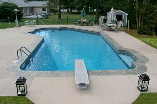 Lazy L style custom inground swimming pool with a black fence, steps and diving board by Cypress Pools